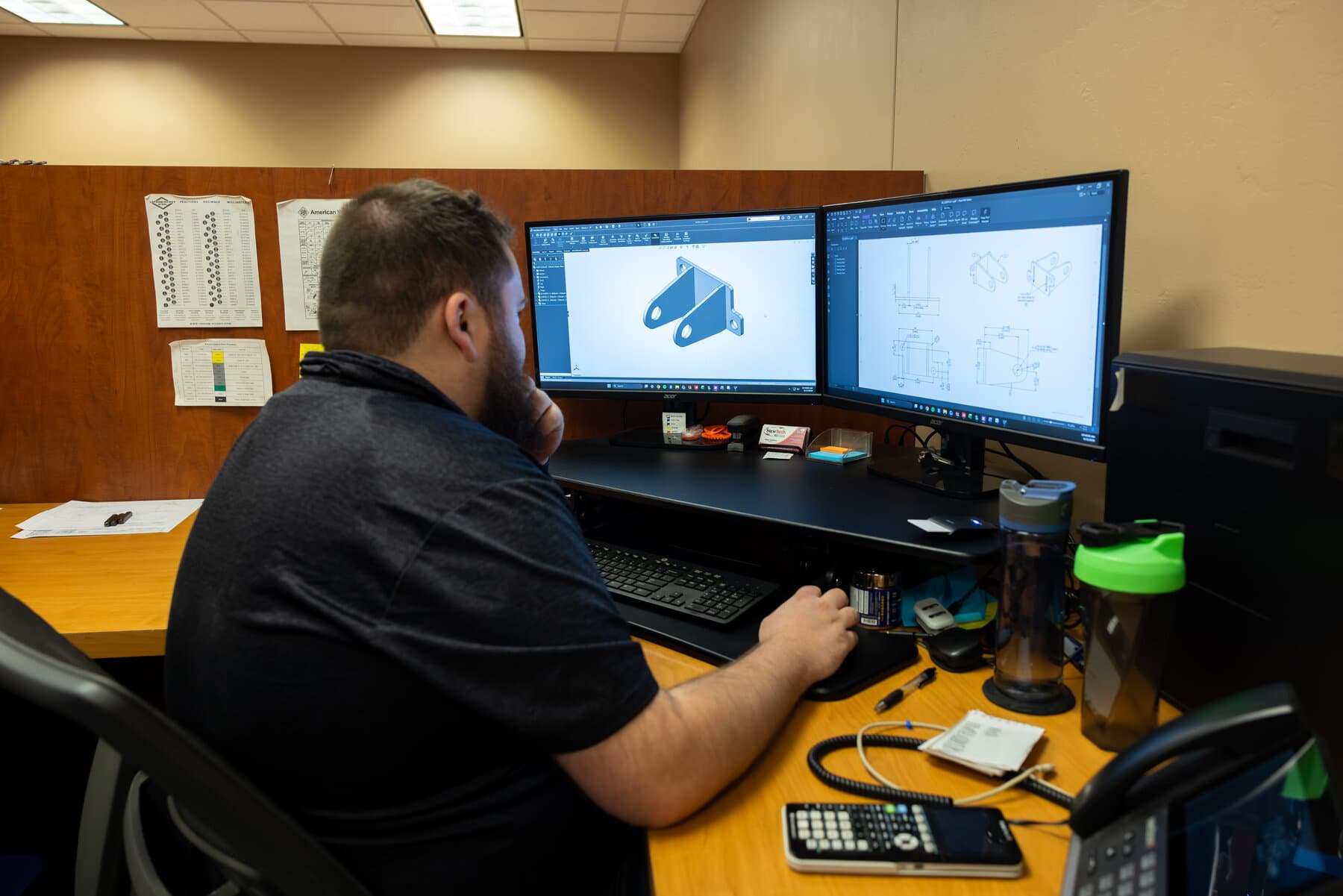 New Tech Metals engineer modeling a bracket in CAD with a 2D drawing on the second monitor