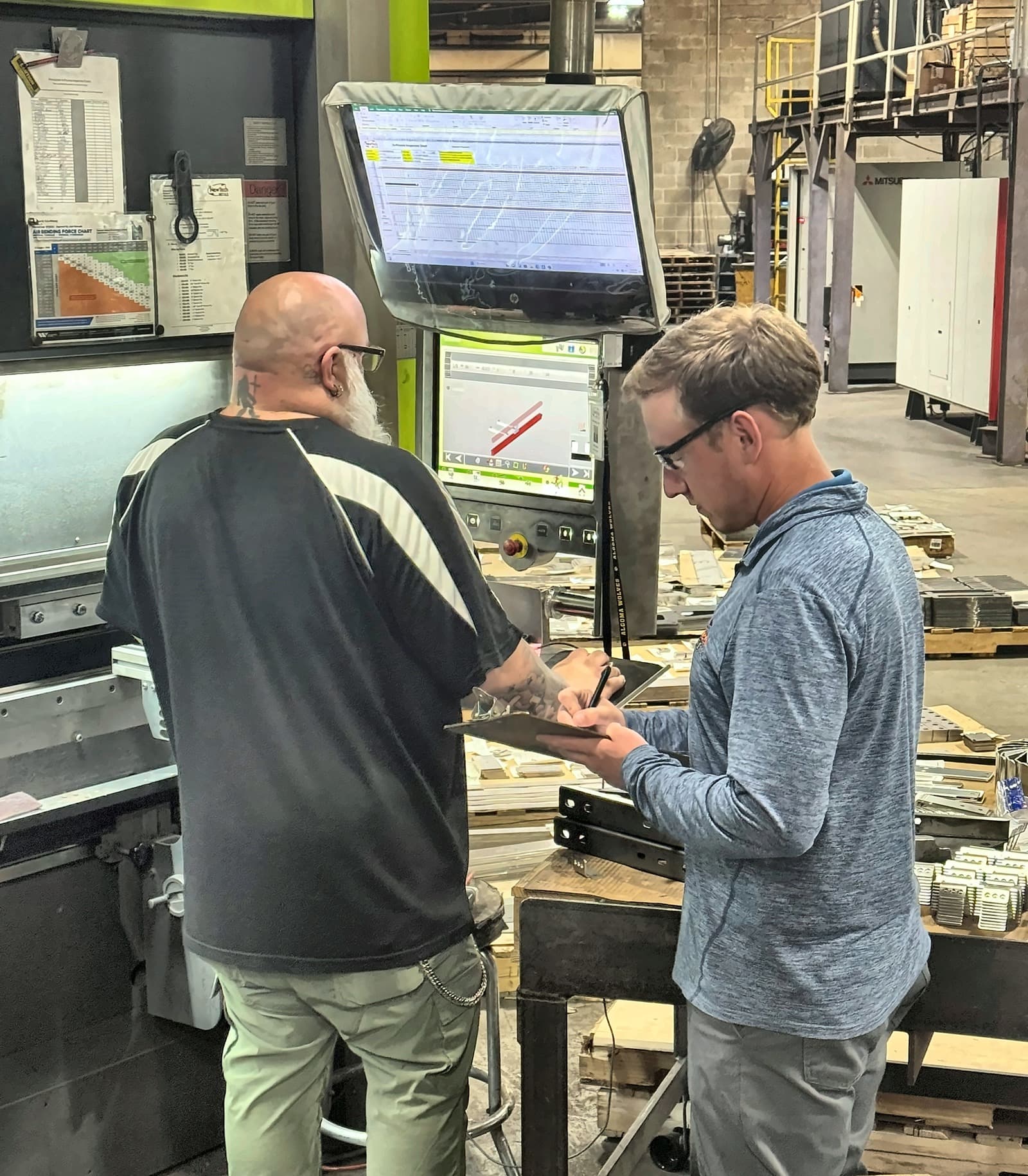 Two New Tech Metals operators reviewing a job at the press brake