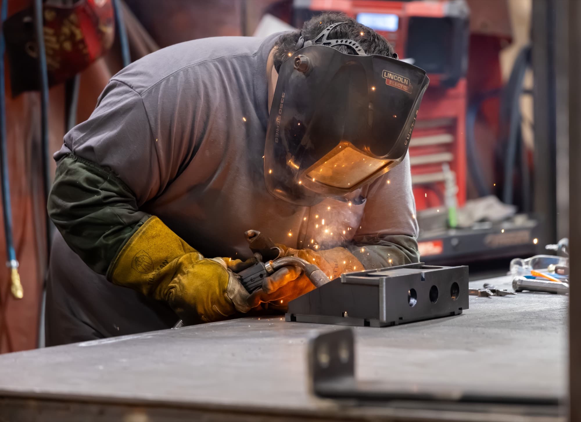New Tech Metals welder MIG welding a steel part at the fabrication bench with sparks flying