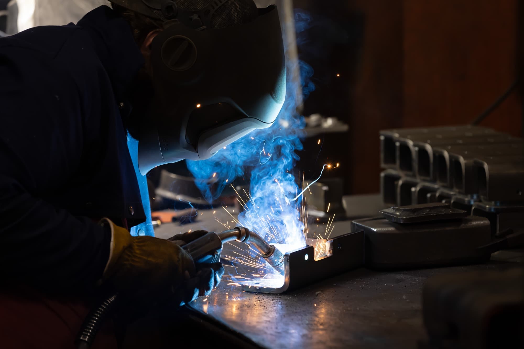 New Tech Metals welder MIG welding a mild steel component with blue arc smoke and sparks